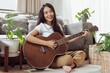 Woman playing guitar at home. Beautiful woman smiling and playing guitar with her plants in living room.