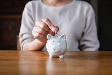 Wall Mural - Closeup image of a woman putting coins into piggy bank for saving money concept