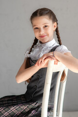 Wall Mural - Portrait of a schoolgirl in a school uniform sitting on a chair.