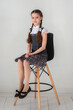 Portrait of a schoolgirl in a school uniform sitting on a chair.
