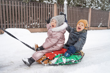 Wall Mural - In winter, in the snow, happy brother and sister go sledding