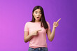 Leinwandbild Motiv Excited alarmed cute asian female describe shocking scene pointing right, show index fingers sideways thrilling event, discuss amazing performance look camera worried, stand purple background