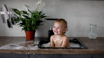 cute happy baby girl with playing with water and foam in a kitchen sink at home