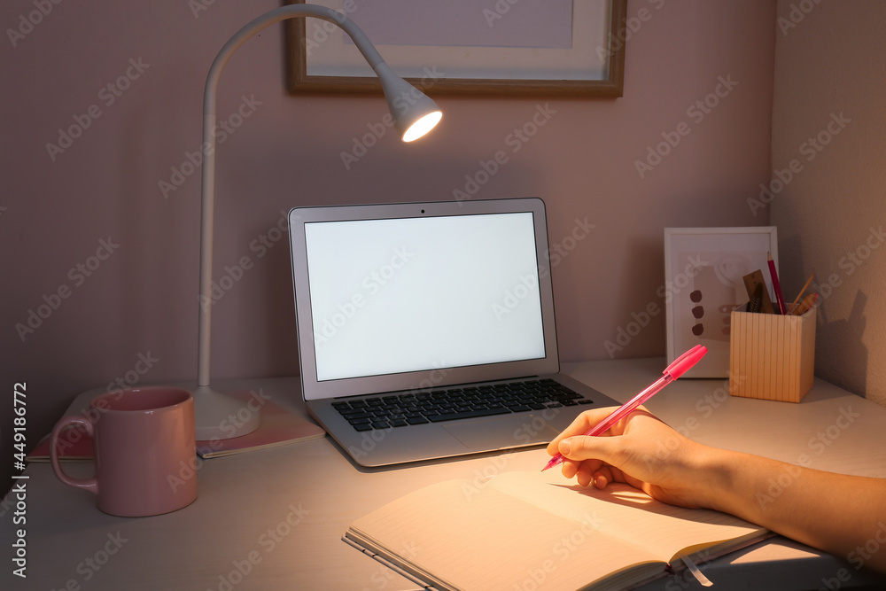 Woman writing in notebook at home late in evening