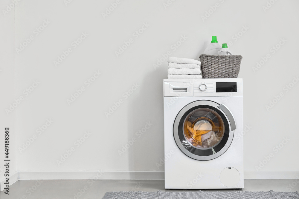 Modern washing machine with laundry near light wall