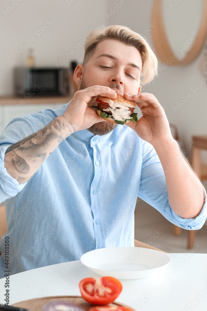 Young man eating vegan burger in kitchen