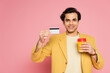 © LIGHTFIELD STUDIOS - happy young man holding credit card and paper cup on pink