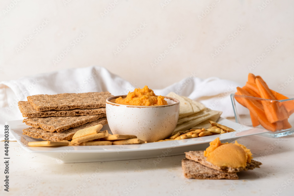 Bowl with tasty carrot hummus and crackers on light background