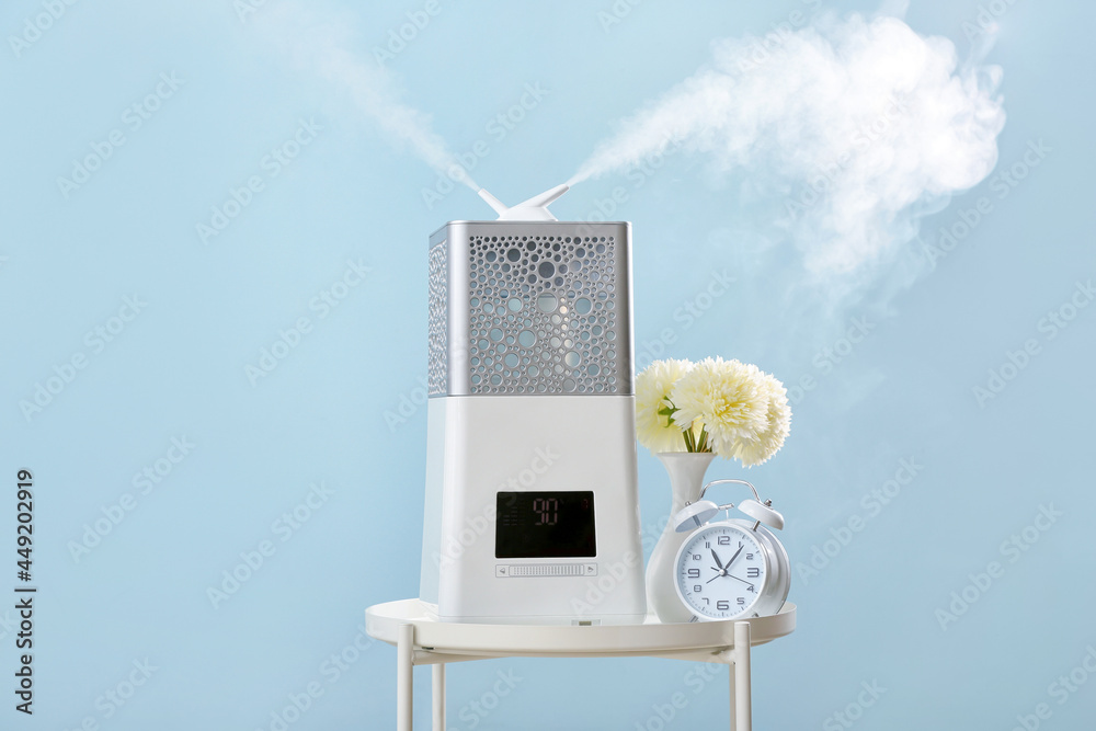 Modern humidifier, vase and alarm clock on table against color background
