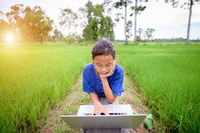 Asian Girl Living In Rural Areas And Schools In Rural Areas Of Thailand Elementary School Children Are Studying Online At Home In Rice Fields Using Laptops To View Teaching Materials.