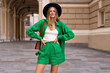 Elegant stylish woman posing at Paris street wearing green linen suit and black fedora, summer vacation style.