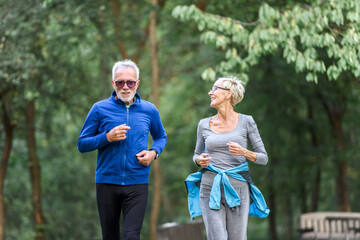 Wall Mural - Smiling senior couple jogging in the park. Sports activities for elderly people.