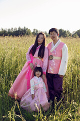 Korean family in national costumes is stand in a field at sunset