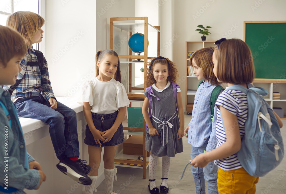 Shy elementary school children meeting each other for first time with school bags in classroom