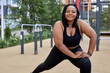 © Roman - adorable fat woman in black tracksuit is engaged in fitness on sports ground, side view portrait. Young african overweight woman lunges outdoors on warm summer day. Healthy lifestyle, weight loss.