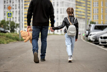 Pedophile Man Holds The Hand Of Teenage Girl In Street. The Concept Of Kidnapping And Child Trafficking. Rear View On Pedophile With Toy And Caucasian Child Girl Walking Along The Street. Crime