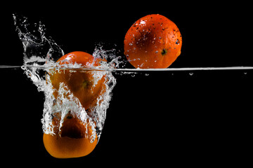 three tangerines fall into the water on a black background, copy space