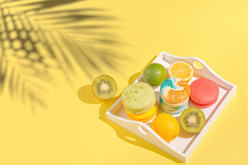 Wall Mural - Colorful macaroons with lemon, lime  and kiwi on white tray on sulit yellow background with shadows . Summer refreshment concept.