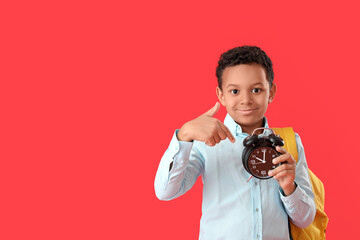 Wall Mural - Little African-American schoolboy pointing at alarm clock on color background