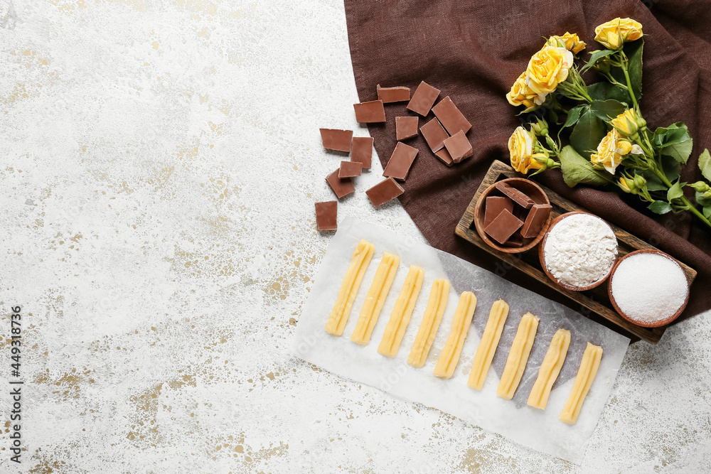 Uncooked churros, ingredients and flowers on light grunge background