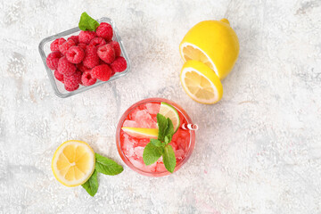 Glass of cold lemonade, bowl with raspberry and sliced lemon on light background