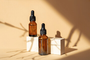 Mock-up of two glass dropper bottles standing on wooden geometric stand. Hard shadows from branch fall on surface of object. Concept of 3d podium for demonstrating cosmetic packaging