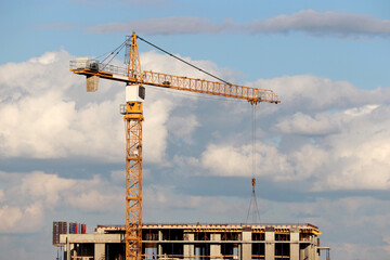 Wall Mural - Construction crane and unfinished residential building on background of blue sky with white clouds. Housing construction, apartment block in city