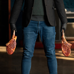 Man in jeans holds t-bone steaks. Butcher holding two large pieces of raw meat on bone. Blurred background. Close-up shot.