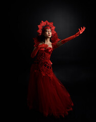 Wall Mural - Full length  portrait of beautiful young asian woman wearing red corset, long opera gloves and ornate gothic queen crown. Graceful posing isolated on a dark studio background.