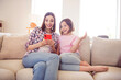© deagreez - Portrait of two attractive cheerful girls sitting on divan using device gadget having fun at home flat indoors