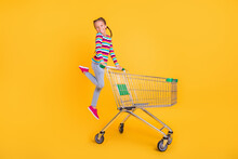 Photo Of Funny Girl Jump Move Trolley Shopping Wear Striped Shirt Jeans Shoes Isolated Yellow Color Background