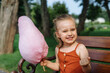 © kaloriya - Beautiful little girl eating pink cotton candy in the park.