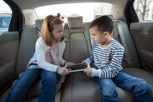 Brother And Sister Fighting Over Digital Tablet On The Back Seat Of The Car