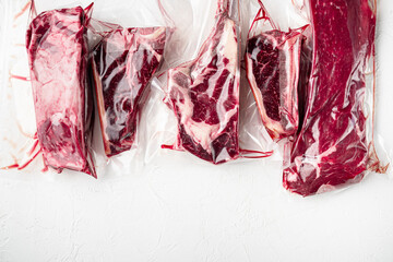 Wall Mural - Vacuum packed organic raw beef classic cuts, tomahawk, t bone, club steak, rib eye and tenderloin cuts, on white stone  background, top view flat lay, with copy space for text