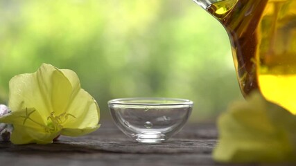 Wall Mural - Slow motion of pouring evening primrose oil from a bottle, with fresh Oenothera biennis flowers in the background