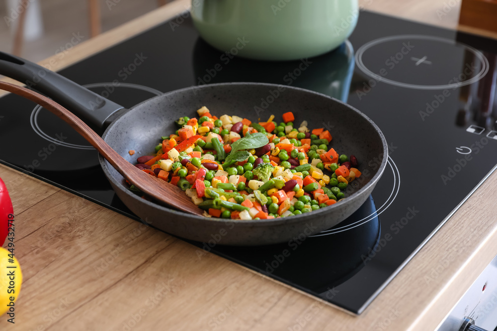 Frying pan with tasty vegetables on stove in kitchen
