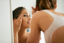 Young Beautiful Woman Looks Her Face Skin In Mirror At Home.