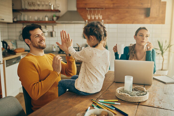 Wall Mural - Playful father and daughter give high-five and have fun while mother is working at home.