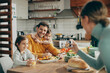 © Drazen - Happy father and daughters have fun while mother photographing them during a meal at dining table.