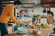 © Drazen - Happy parents use touchpad while preparing lunch with their daughters at home.