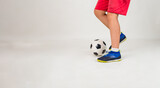 Fototapeta Sport - close-up of a boy in a red football uniform playing a ball on a white background with a place for text