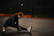 © alfa27 - Motivated redhead female athlete stretching legs for warming up before urban fitness and running workout at night in city, on road. Sporty woman exercising outdoors, side view portrait. copy space
