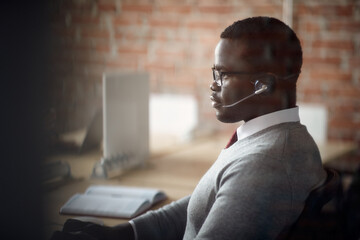  African American entrepreneur with headset works on computer at corporate office.