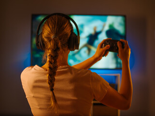 Wall Mural - Girl shooter plays with friends online in an exciting video game. Close-up. Shooting from the back. Evening relaxation, virtual communication with friends, advertising, gaming business.