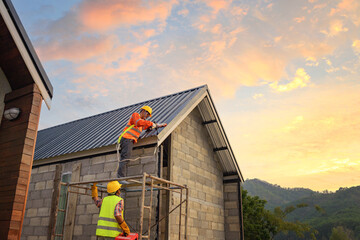 Roofer working on roof structure of building on construction site,Roofer using air or pneumatic nail gun and installing Metal Sheet on top new roof.