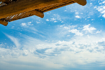 Wall Mural - (Selective focus) Stunning view of a blue sky with some clouds during a sunny day and a wooden roof in the foreground. Natural background with copy space.