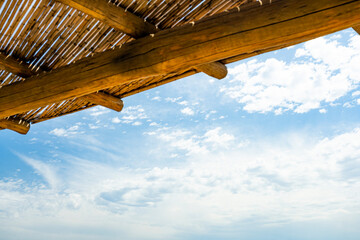 Wall Mural - (Selective focus) Stunning view of a blue sky with some clouds during a sunny day and a wooden roof in the foreground. Natural background with copy space.