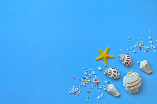 A corner of a blue background filled with seashells, a starfish, and colorful pebbles, copy space