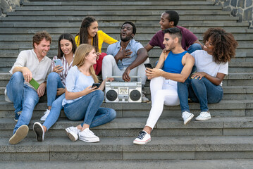Wall Mural - Young multiracial friends having fun listening music with vintage boombox stereo and using mobile smartphone while sitting on urban stairs - Youth millennial lifestyle concept