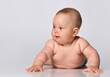 six-month-old baby in one diaper stands up on the arms and looks to the side, against a light background.